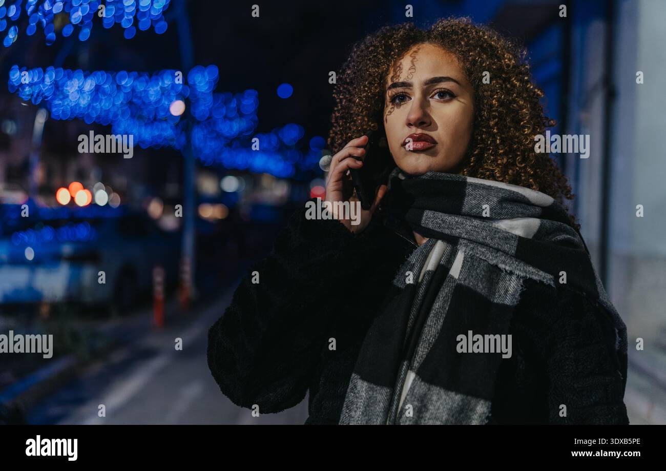 Porträt einer Frau am Telefon bei Nacht unter blauer Stadtbeleuchtung Stockfoto