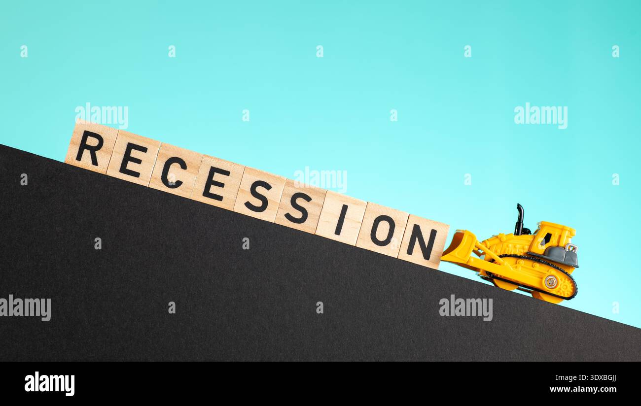 Ein gelber Bulldozer verhindert, dass Holzbuchstaben, die das Wort „Rezession“ ausdrücken, nach unten rutschen. Die Szene symbolisiert eine negative wirtschaftliche Phase. Stockfoto