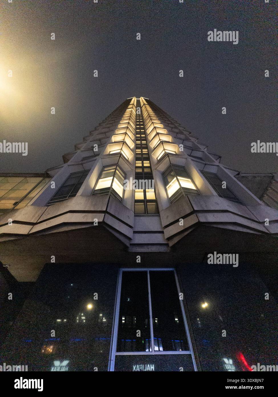 Nachtsicht in flachem Winkel auf den beleuchteten Centre Point Tower in London, eckige, brutalistische Betonfassade mit leuchtenden Fenstern vor dunklem Himmel Stockfoto