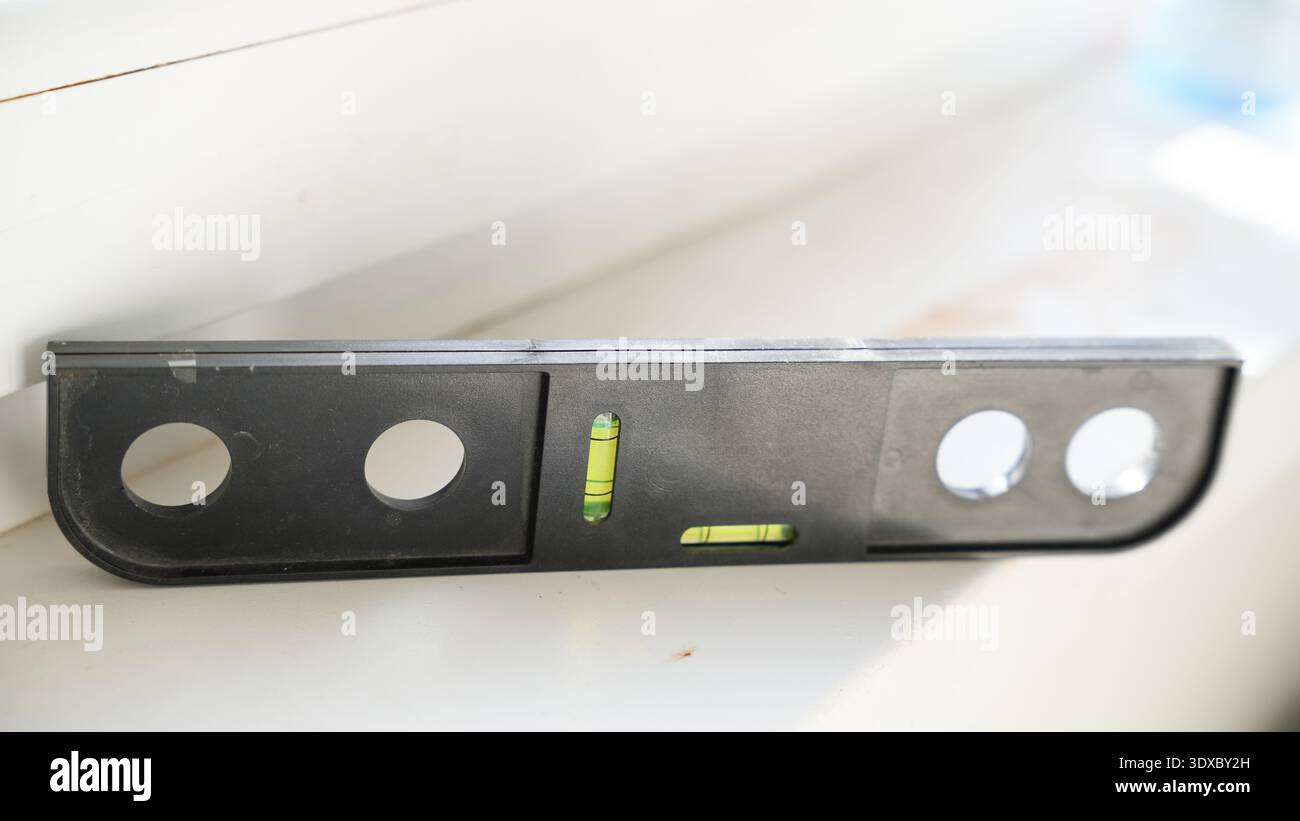 Schwarze Wasserwaage auf einer weißen Oberfläche zur Ausrichtung bei Installations- oder Renovierungsarbeiten. Stockfoto