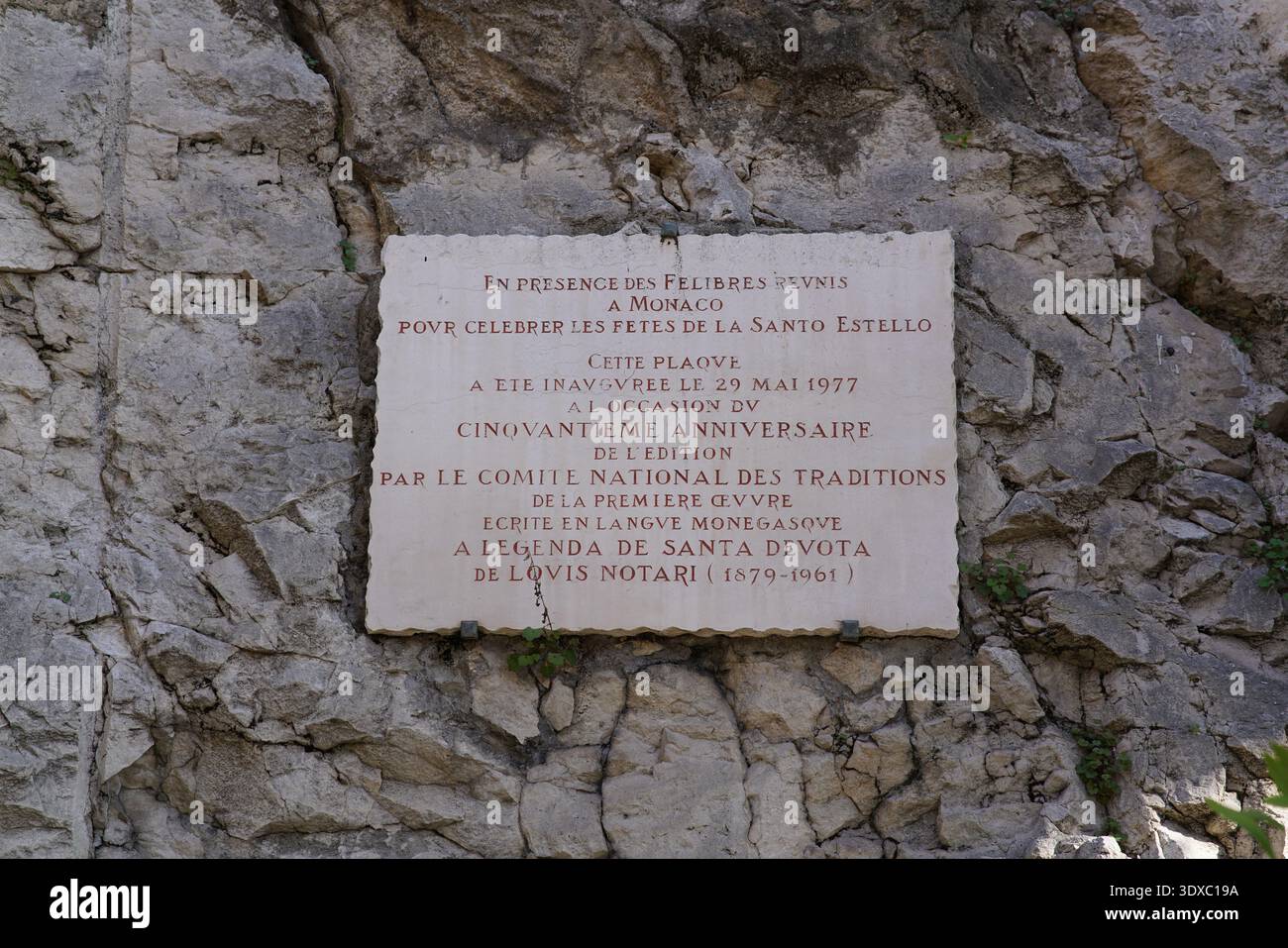 Historische Gedenktafel an der Felsmauer an der Chapelle Sainte-devote in Monaco zum Gedenken an die Traditionen von Santa Devota und 1977. Jahrestag. Monte Carlo, Monaco Stockfoto