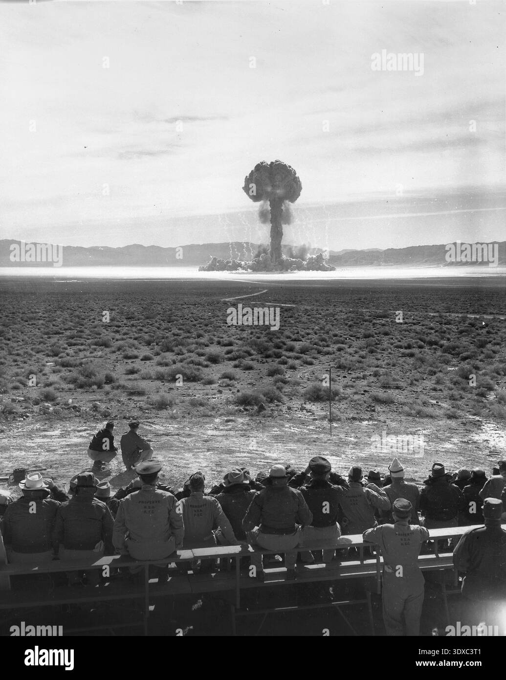 Personal, das die Detonation von Projekt 'Open Shot', Nevada, April 1952 beobachtet hat. Mitarbeiter der Militär- und Atomenergiekommission beobachteten den „Open Shot“-Atomtest im April 1952 auf dem Nevada Test Site während der Operation Tumbler. Bei dieser Veranstaltung wurde ein Gerät gezündet, um die Auswirkungen auf verschiedene Strukturen zu testen, darunter unterirdische und oberirdische Versorgungsunterstände, die sich in unterschiedlichen Abständen von Ground Zero befinden. Eine optimierte Version eines historischen Archivdokuments. Quelle: US-Energieministerium. Stockfoto
