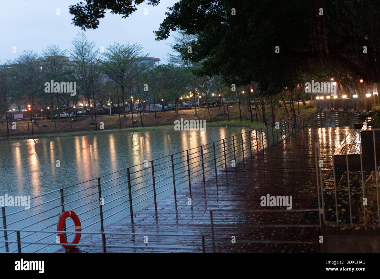 Verregneter Abendspaziergang entlang der nassen Promenade am See in Taipei, Taiwan mit Reflexionen und Lebenshilfe Stockfoto