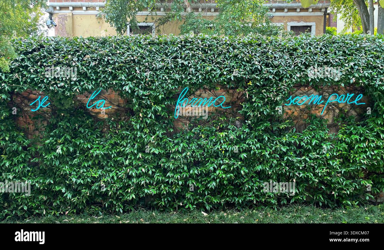 Ein blaues Neontextwerk von Mario Merz leuchtet auf einer mit Efeu bedeckten Wand in der Peggy Guggenheim Collection in Venedig, Italien. Stockfoto