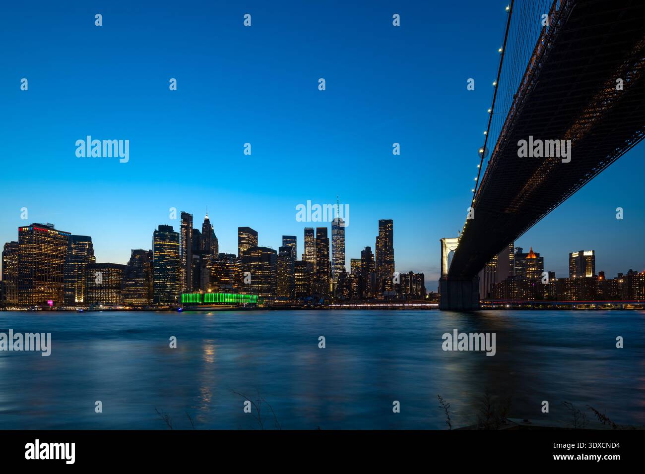 Die architektonische Größe der Brooklyn Bridge bietet einen atemberaubenden nächtlichen Blick auf den urbanen Horizont von Manhattan. Stockfoto