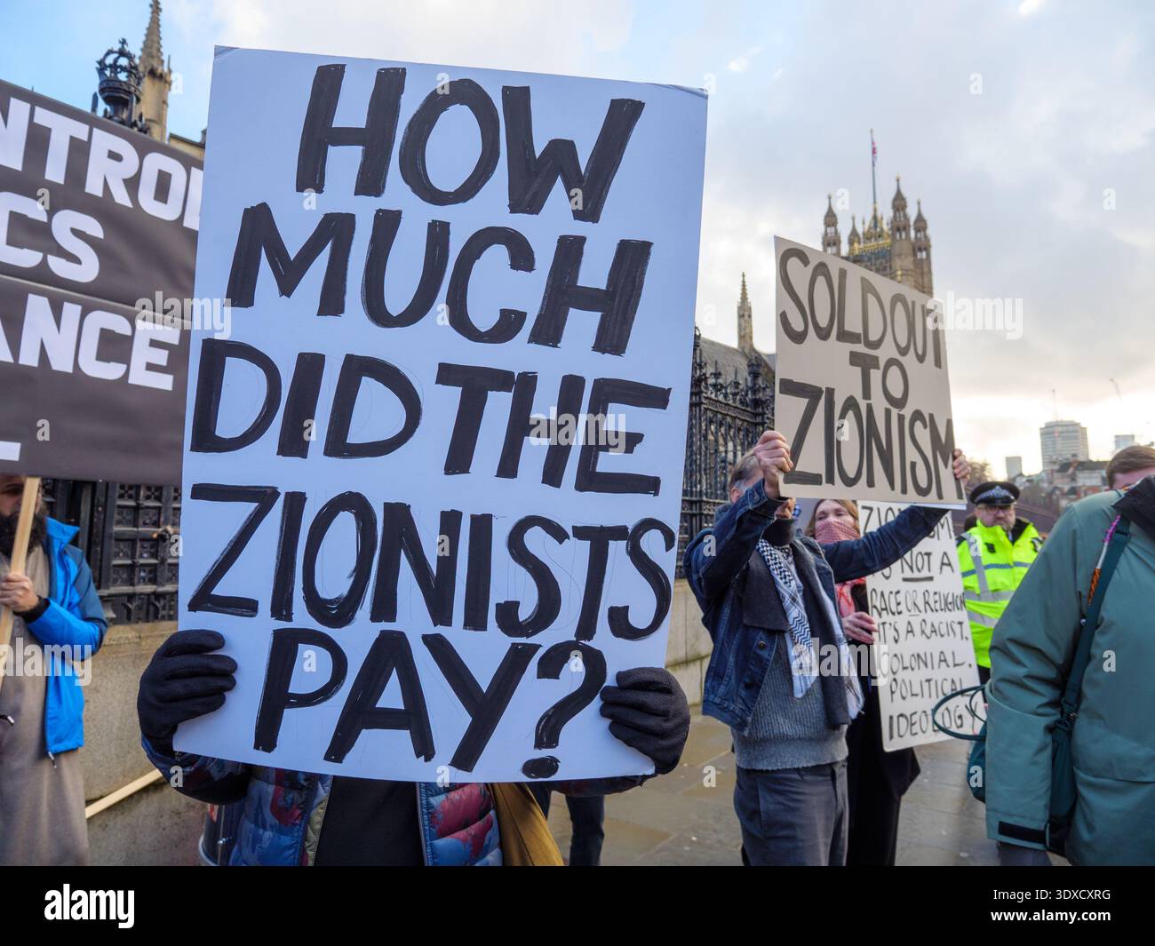 Antizionisten halten Schilder, die die antisemitische Verschwörung über die jüdische Macht bei einem Protest vor den Houses of Parliament in London, Großbritannien, vorantreiben Stockfoto