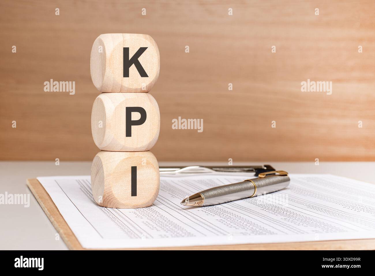 Vorderansicht von drei hölzernen Spielzeugblöcken mit der Schreibweise KPI, die vertikal auf einem Schreibtisch mit Stift und Bericht gestapelt sind. Konzept der Schlüsselleistung Stockfoto
