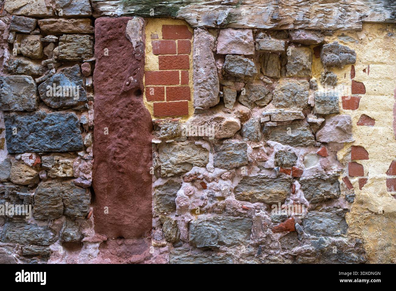 Vollrahmen-Textur einer alten Flickenteppichmauer, eine Mischung aus rustikalen Steinen, roten Ziegeln und verwittertem Mörtel mit einem Holzbalken an der Spitze in einem mittelalterlichen Stockfoto
