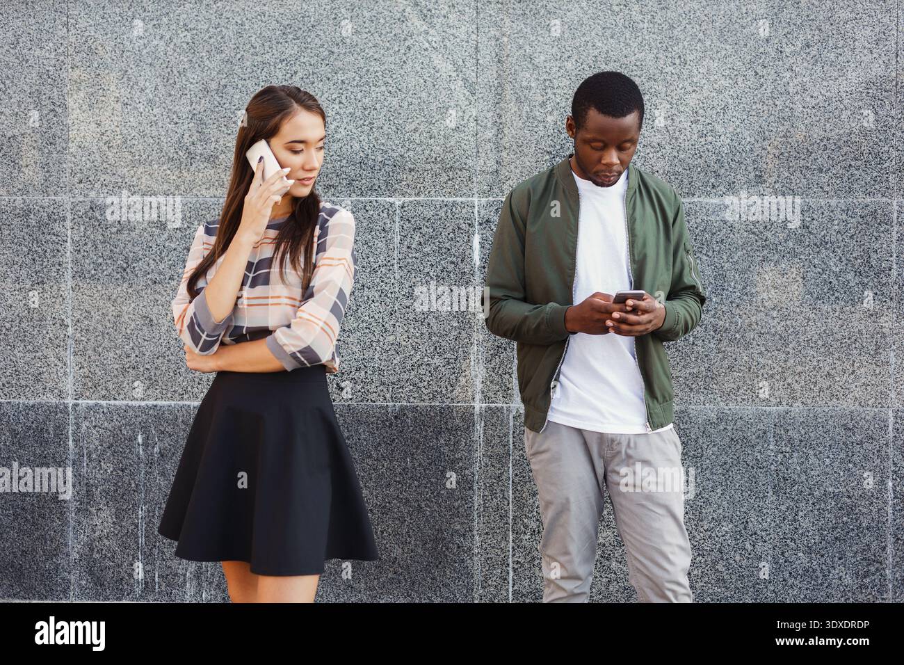 Zwei Personen nutzen tagsüber Telefone vor einer grauen Mauer in einer städtischen Umgebung Stockfoto