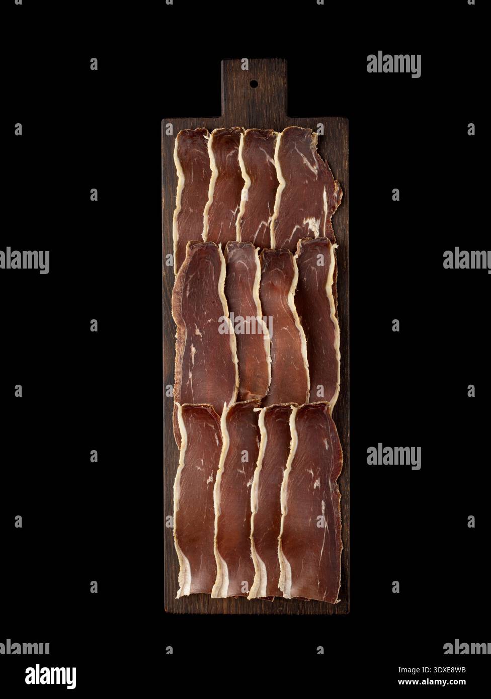 Dünn geschnittenes Fleisch, einschließlich Marmelade, kunstvoll auf einem rustikalen dunklen Holzschneidebrett angeordnet. Isoliert auf schwarzem Hintergrund, Draufsicht. Stockfoto