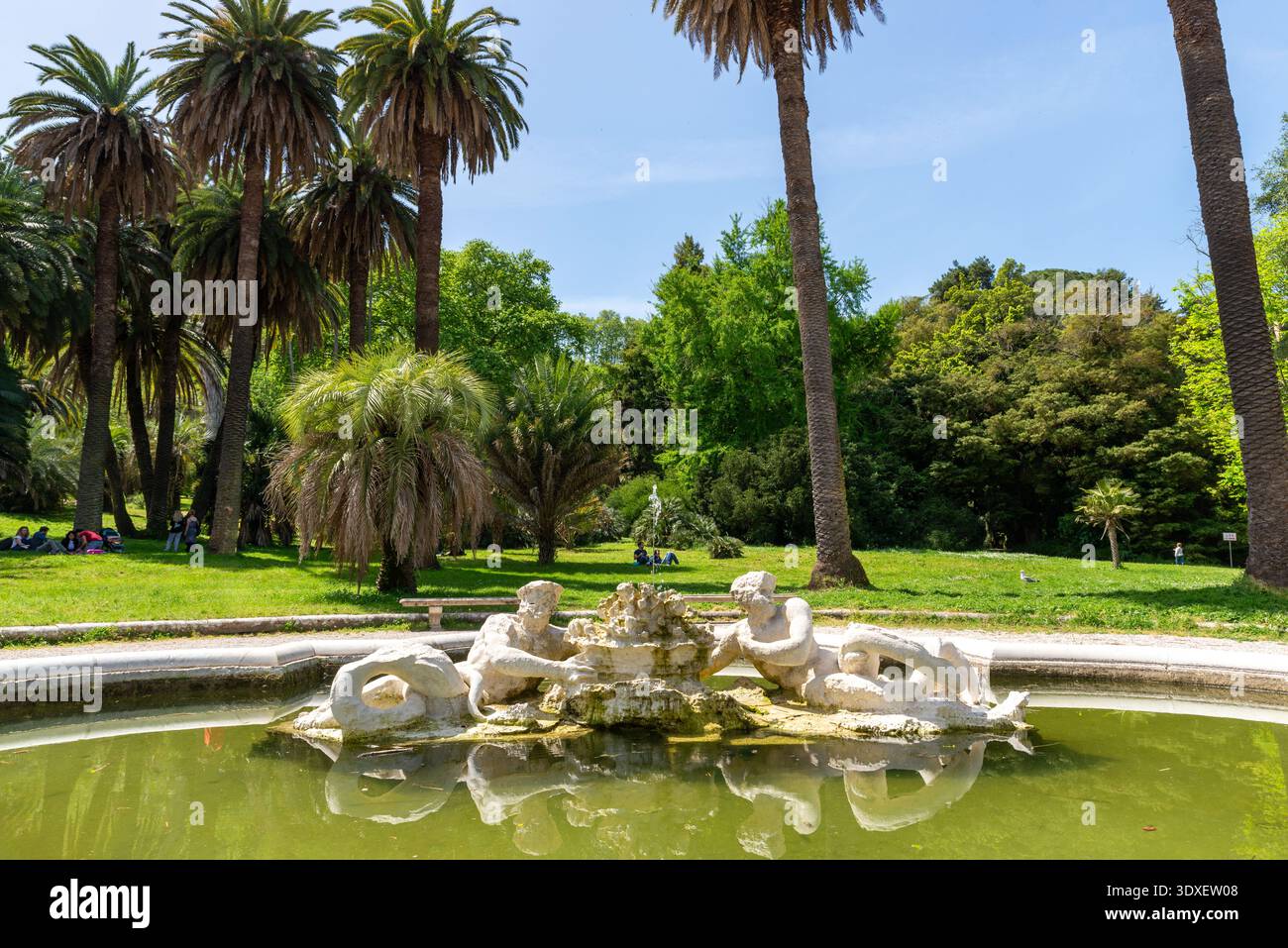 Rom, Italien – 21. April 2025: Kleiner, dekorativer Brunnen in einem von Palmen gesäumten Park, in dem Besucher auf grünen Rasenflächen im Hintergrund entspannen können Stockfoto