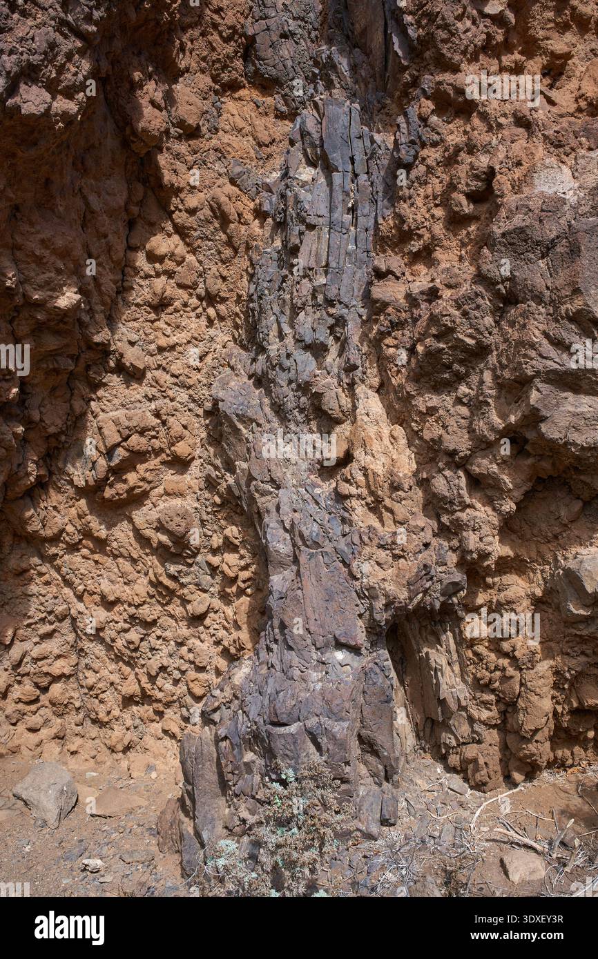 Nahaufnahme der dramatisch gestuften roten und ockerfarbenen vulkanischen Klippen mit kontrastierenden Basaltfelsen-Texturen und spärlicher endemischer Vegetation in der Anaga Re Stockfoto