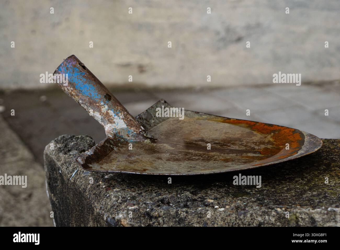 Rostiger Mauerwerkskelle auf einer Betonoberfläche mit abgenutztem Metall, Korrosion und Anzeichen von Bauarbeiten. Stockfoto