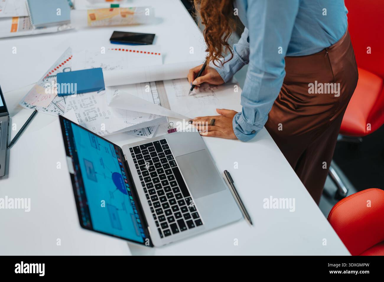 Designer an einem aufgeräumten Schreibtisch, der Blaupausen mit Laptop und Papieren entwirft und Skizzen plant Stockfoto