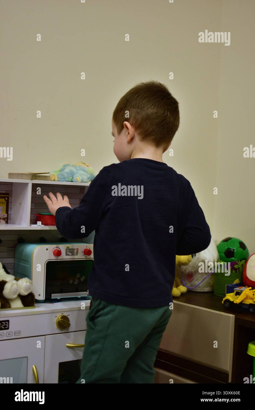 Kleinkind Junge spielt mit Spielzeugküche zu Hause und tut so, als würde er kochen. Lifestyle-Szene im Innenbereich mit Lernspielzeug, Fantasie-Entwicklung und Kreativität Stockfoto