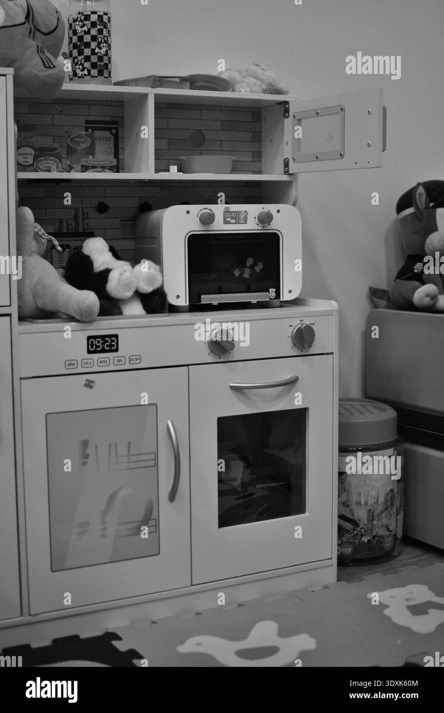 Schwarz-weiß-Bild von Kinderspielzeug Küche Innenraum mit Kuscheltieren und Spielofen. Minimale häusliche Umgebung, die kindliche Vorstellungskraft repräsentiert Stockfoto