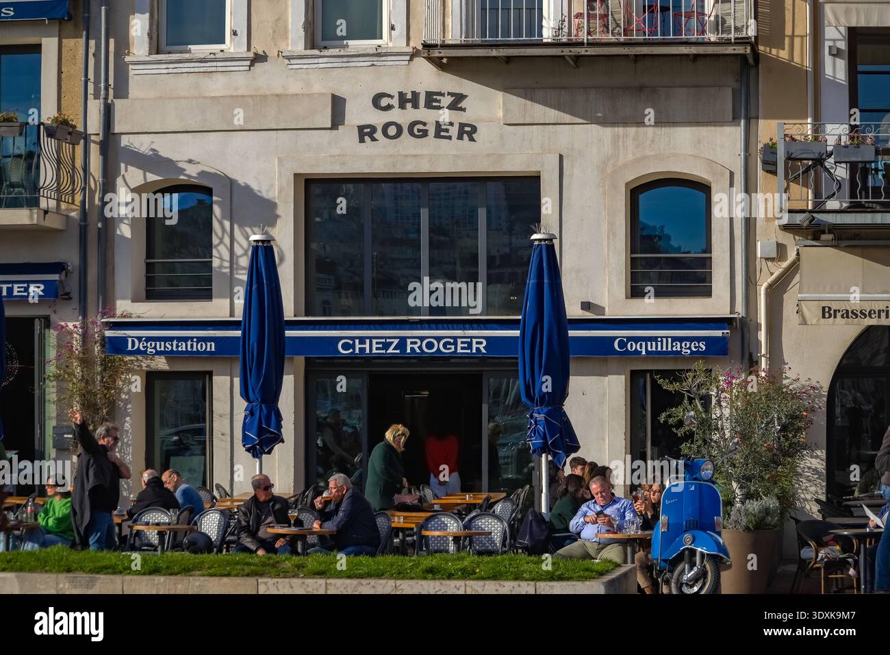 Chez Roger, französische Bistrofassade mit Sitzgelegenheiten im Freien. Essen im Freien, blaue Sonnenschirme und ein klassischer blauer Roller in der Nähe von Marseille, Frankreich Stockfoto
