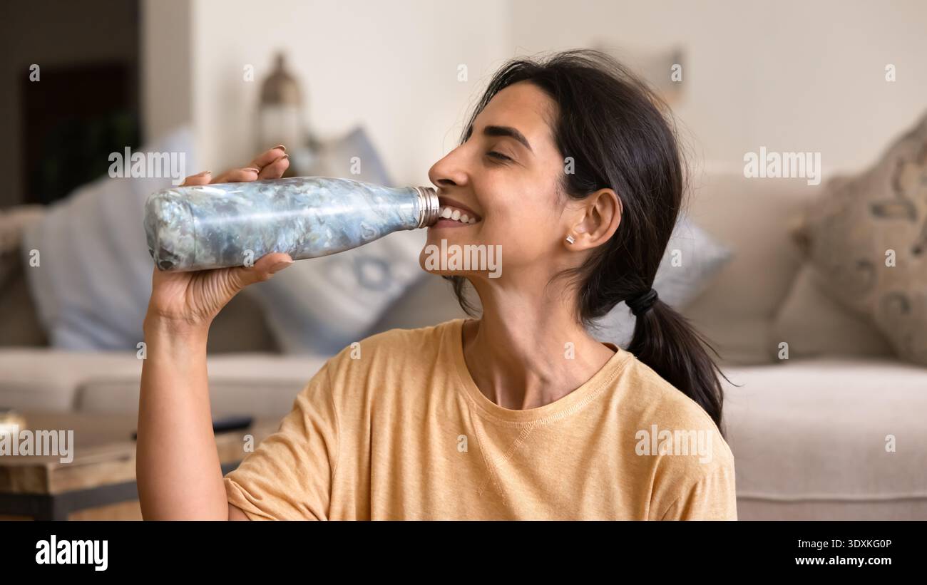 Nahaufnahme einer lächelnden Latina-Frau, die Wasser aus einer wiederverwendbaren Flasche trinkt Stockfoto