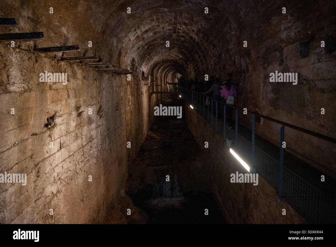 Schwach beleuchteter unterirdischer Steintunnel mit Wasserkanal und Besucherweg in Cazorla, Provinz Jaen, Andalusien, Spanien. Stockfoto