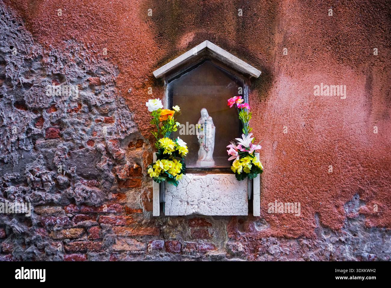Verwitterter Straßenschrein mit Madonnenstatue und Blumen, Venedig, Italien Stockfoto
