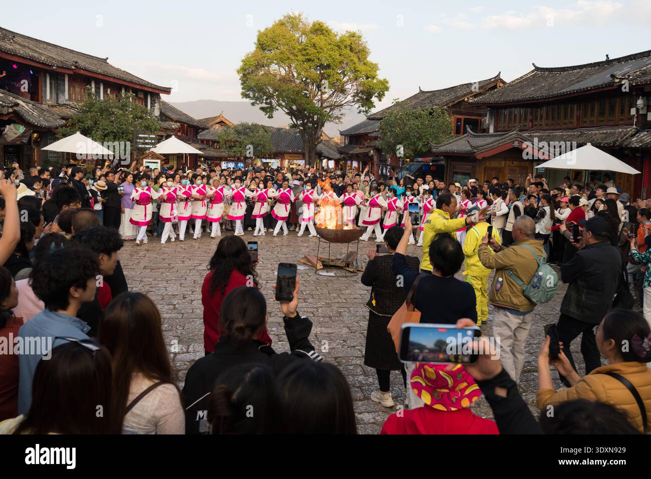 Lijiang, Yunnan, China – 10. April 2025: Naxi-Künstler in traditionellen Kostümen tanzen mit Feuerrequisiten während einer kulturellen Veranstaltung in überfüllten s Stockfoto