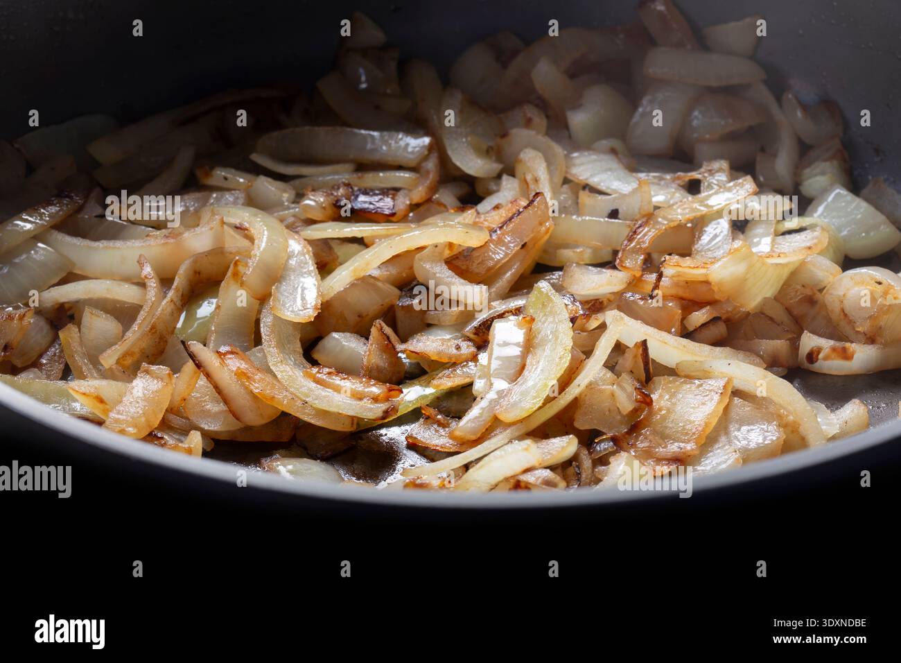 In Scheiben geschnittene weiße Zwiebeln, die in einer tiefen Keramikpfanne im Hintergrund gebraten werden. Stockfoto