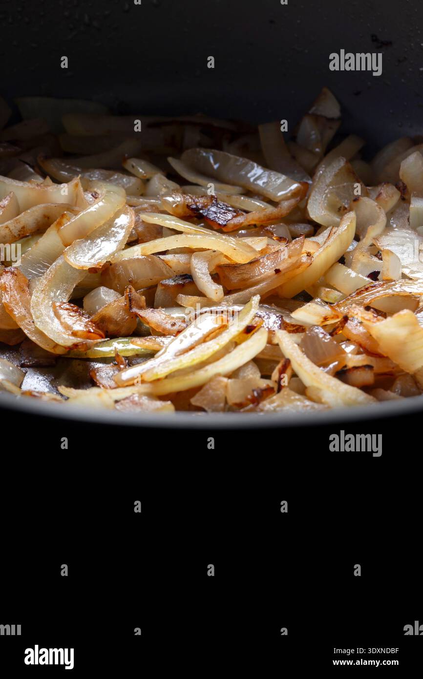 In Scheiben geschnittene weiße Zwiebeln, die in einer tiefen Keramikpfanne im Hintergrund gebraten werden. Stockfoto