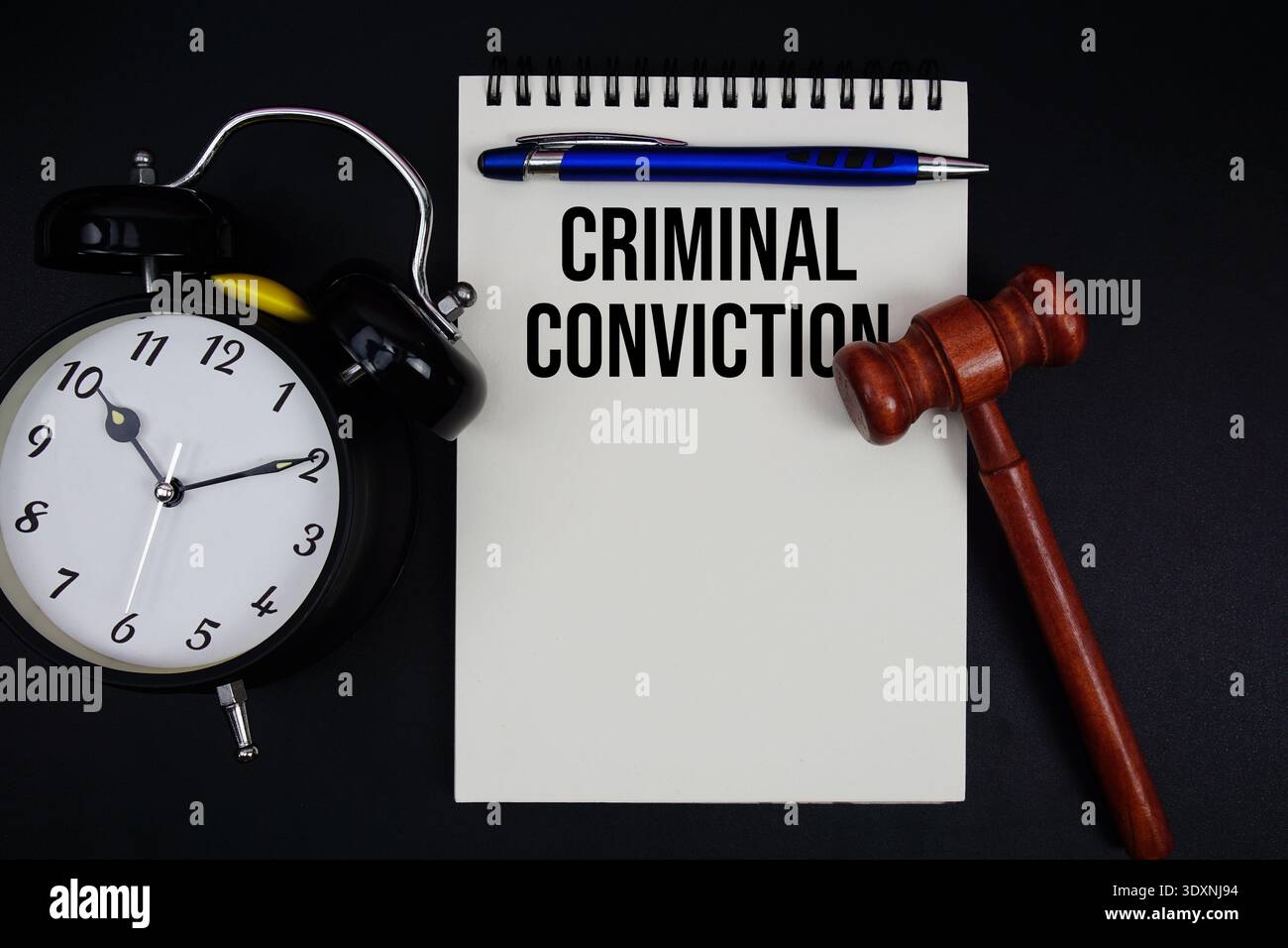 Text der strafrechtlichen Verurteilung auf Notizblock mit Hammer und Wecker auf schwarzem Hintergrund Stockfoto