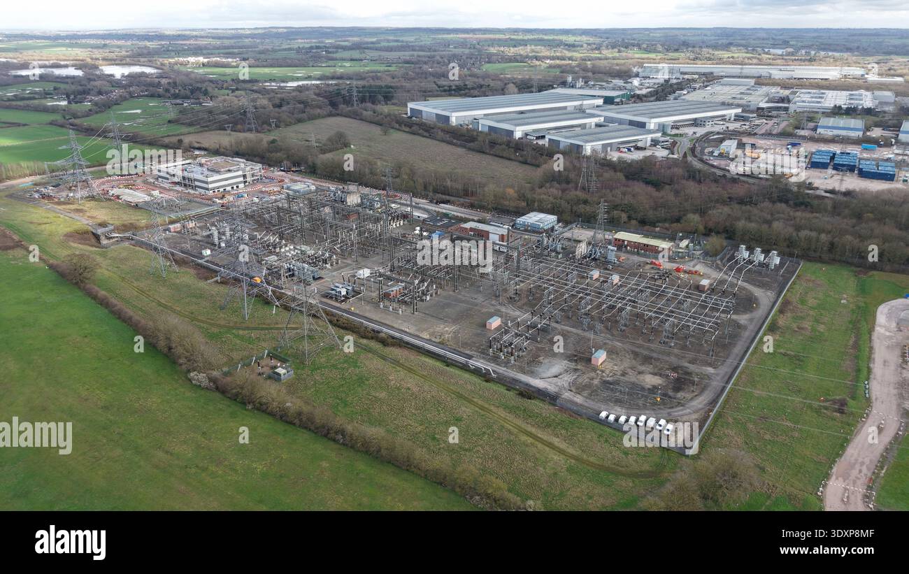Aus der Vogelperspektive eines weitläufigen elektrischen Umspannwerks mit Stromleitungen, die durch die gedämpften Grün- und Brauntöne der umliegenden Landschaft, Birmingham, führen Stockfoto