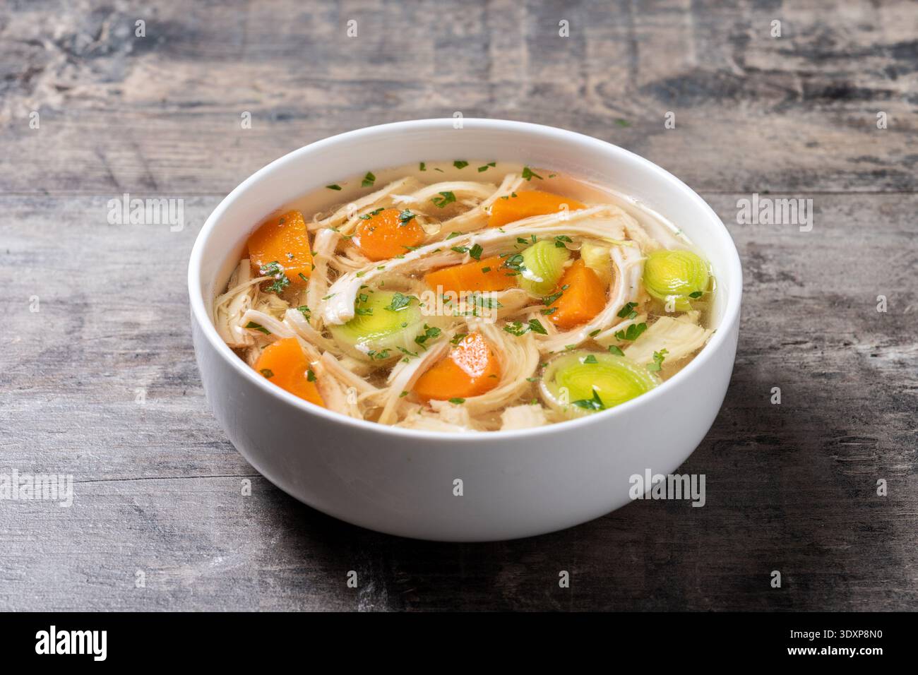 Hausgemachte Hühnersuppe in weißer Schüssel mit Karotten und Sellerie auf weißem Holztisch Stockfoto