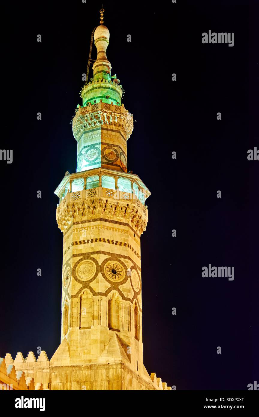 Das Minarett steht nachts in Damaskus hoch. Lichter heben die Details der Struktur hervor. Menschen können sich in der Gegend versammeln. Stockfoto