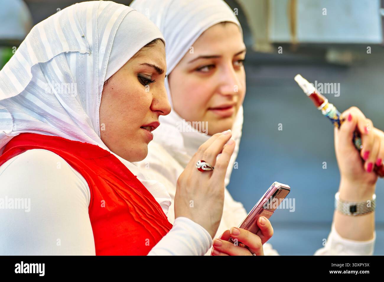 Zwei junge Frauen teilen sich einen Moment in Aleppo, Syrien, rauchen Shisha und benutzen ihre Handys, während sie die Gesellschaft der anderen genießen. Stockfoto