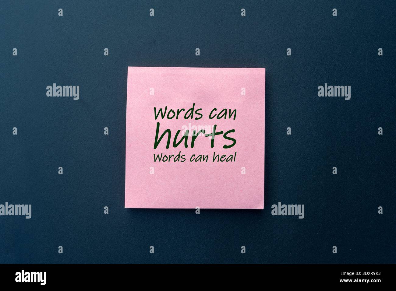 Rosa Haftnotiz mit Text „Words CAN hurts, Words CAN heile“ auf dunkelblauem Hintergrund, der die Kraft der Sprache und der Verdienste um psychische Gesundheit unterstreicht. Stockfoto