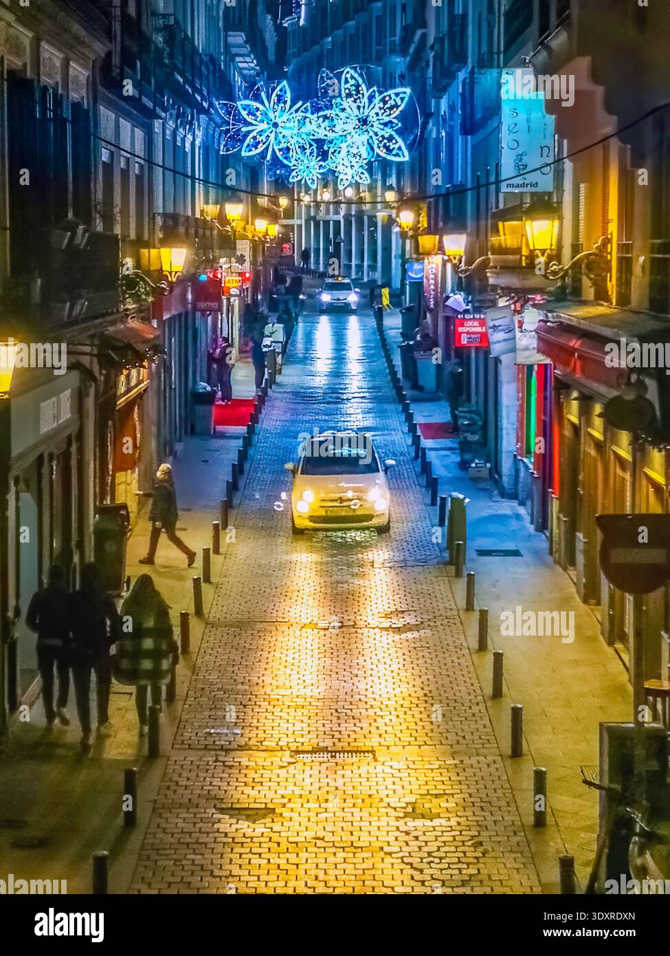 Nächtliche Straßenszene in Madrid während der Weihnachtszeit mit festlichen Lichtern, die eine Kopfsteinpflasterstraße beleuchten. Madrid, Spanien - 30. November 2021 - Smartphone-aufgenommenes Stockfoto