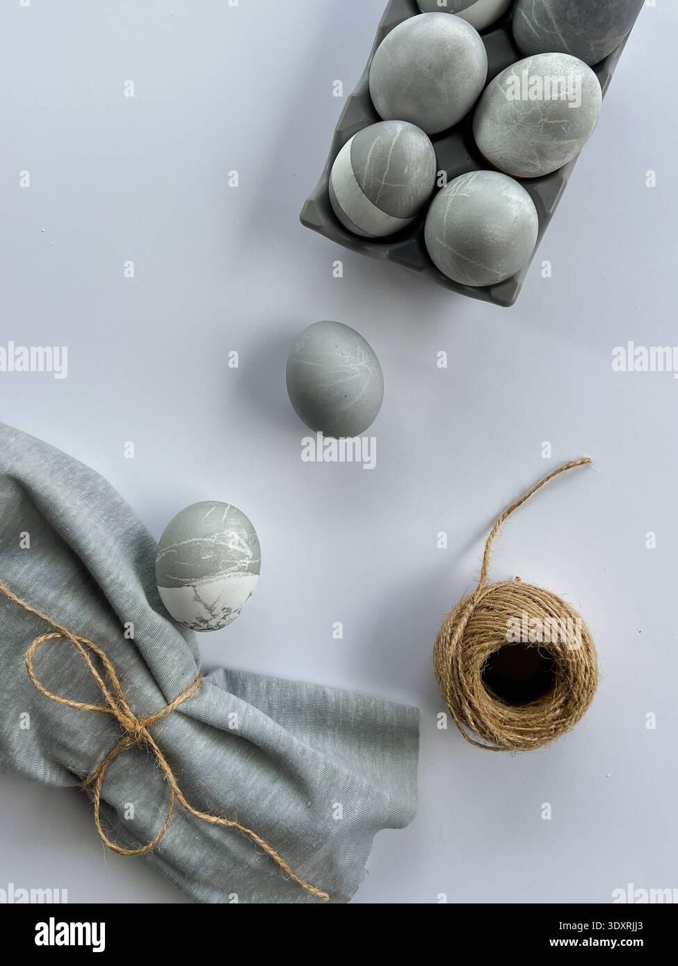 Minimalistisches Osterstilleben mit grauen Marmoreiern, Leinenserviette und natürlichem Garn auf weißem Hintergrund, modernes skandinavisches Urlaubsdekor. Stockfoto
