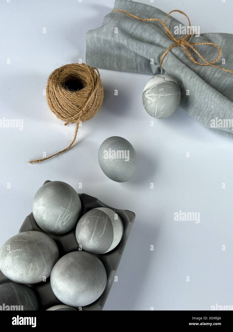 Minimalistisches Osterstilleben mit grauen Marmoreiern, Leinenserviette und natürlichem Garn auf weißem Hintergrund, modernes skandinavisches Urlaubsdekor. Stockfoto