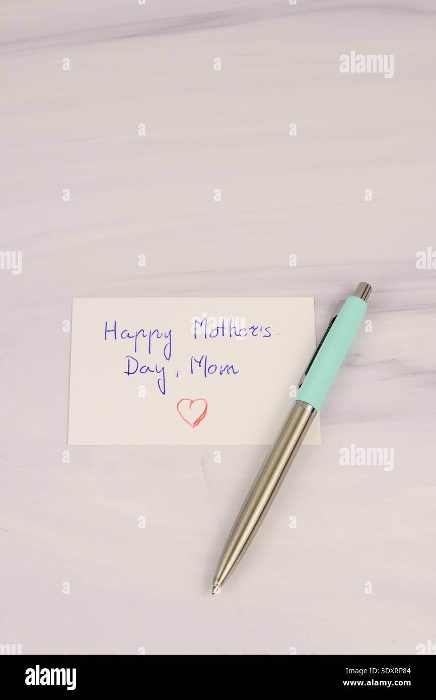 Handgeschriebene Happy Mother's Day-Karte mit Herz und Stift auf weißem Marmorhintergrund. Minimales, flaches Design mit Kopierraum für Begrüßungs- und Liebeskonzept. Stockfoto