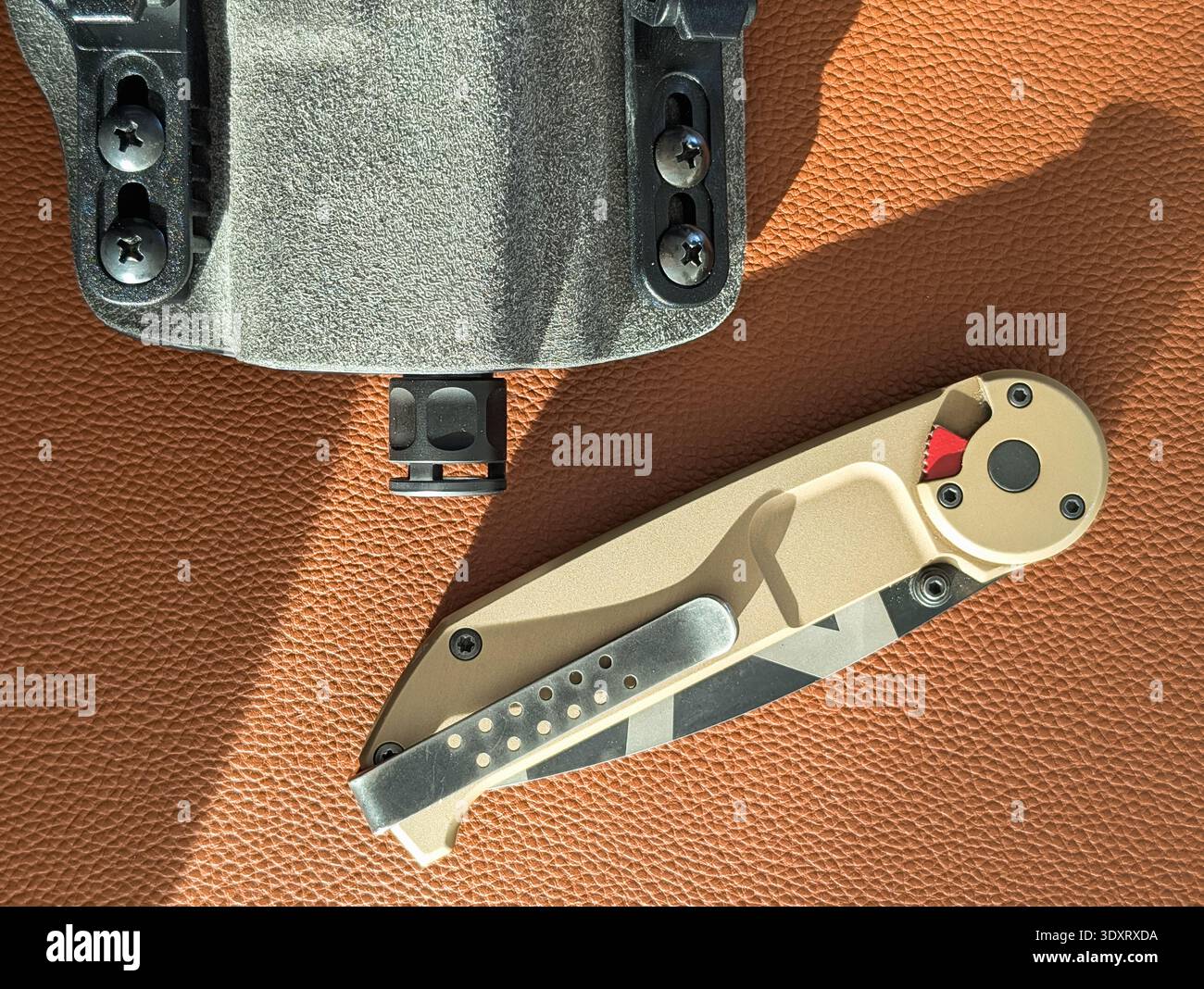 Nahaufnahme des taktischen Klappmessers und der Pistole mit Kompensator im Holster auf brauner Lederoberfläche, EDC-Ausrüstung für den täglichen Gebrauch. Stockfoto