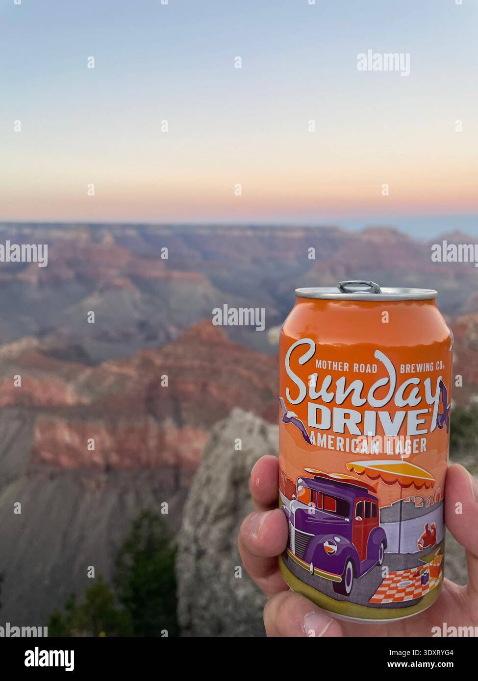 Hand hält eine Dose Craft Beer mit der Landschaft des Grand Canyon im Hintergrund bei Sonnenuntergang, Arizona, USA. - Smartphone-aufgenommenes Stockfoto