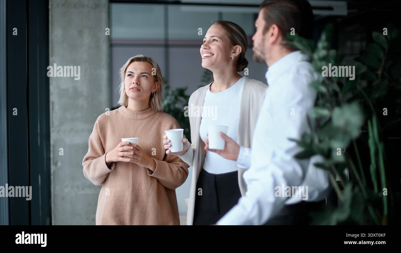 Drei Personen stehen in einem Raum, lächeln und halten Tassen Stockfoto