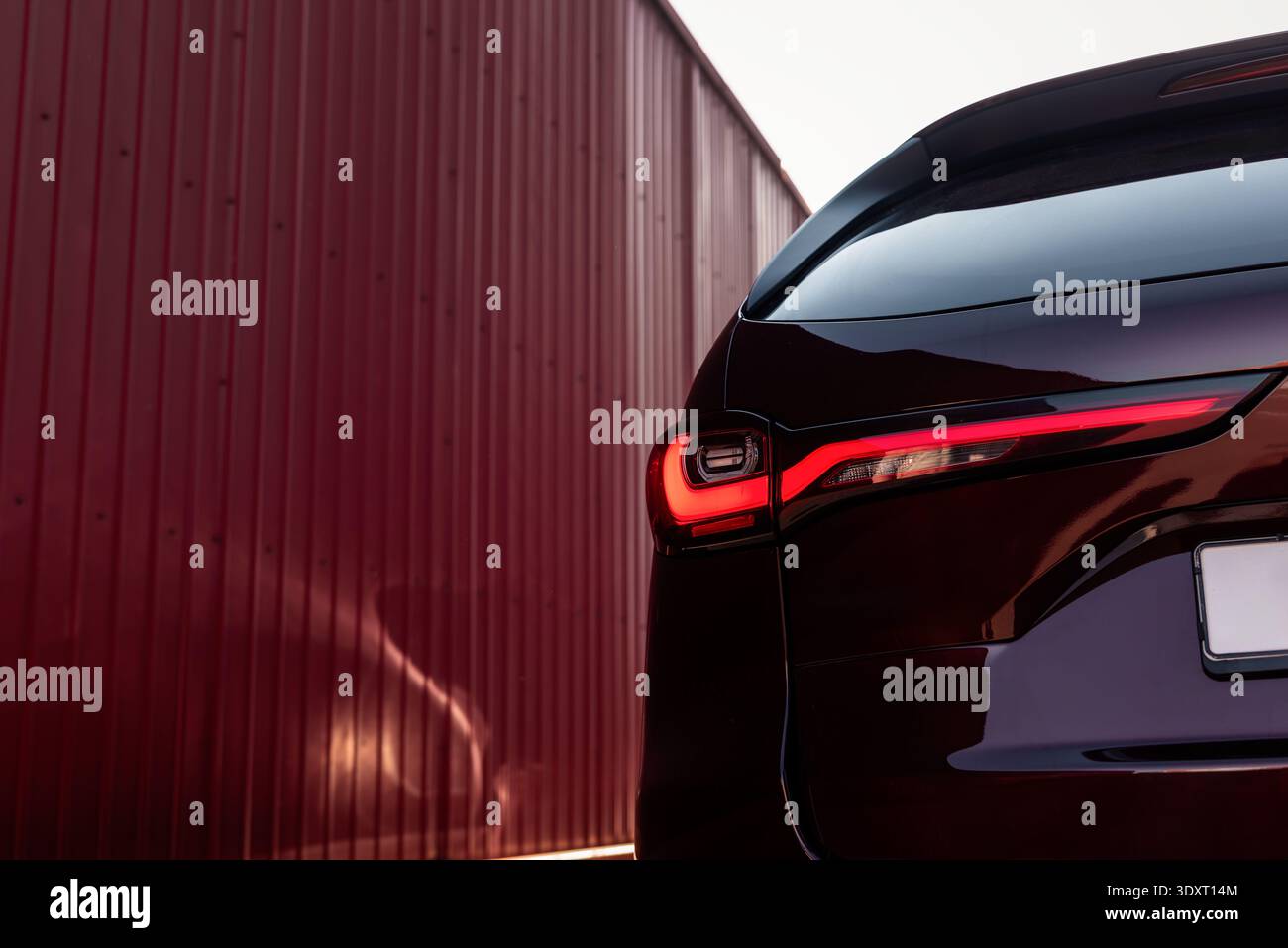 Rücklicht eines modernen Autos an sonnigem Tag. Nahaufnahme des links leuchtenden LED-Rücklichts, rote gewellte Wand im Hintergrund. Stockfoto