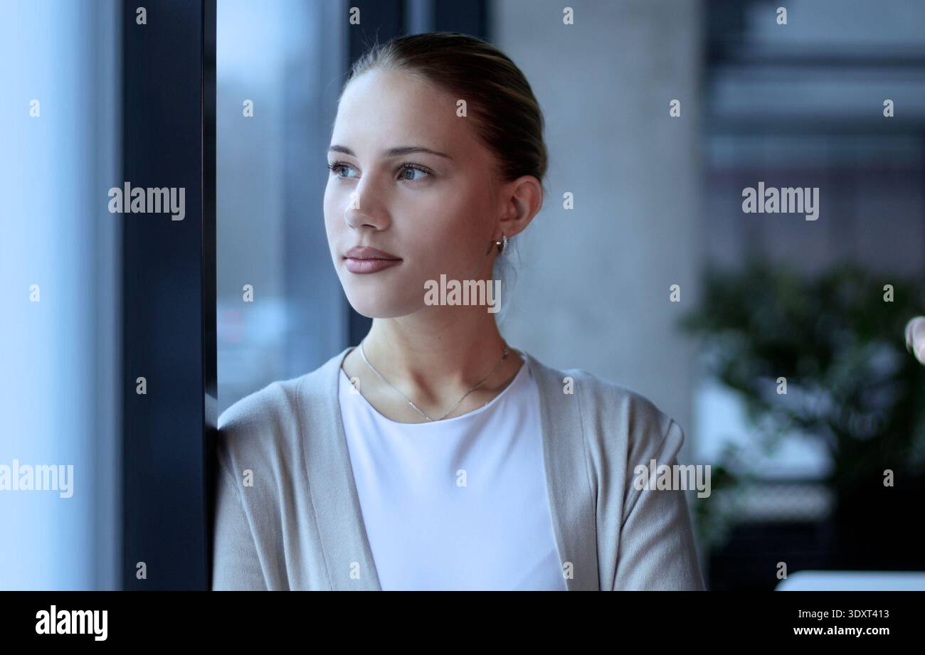 Eine Frau steht vor einem Fenster mit der Hand am Kinn Stockfoto