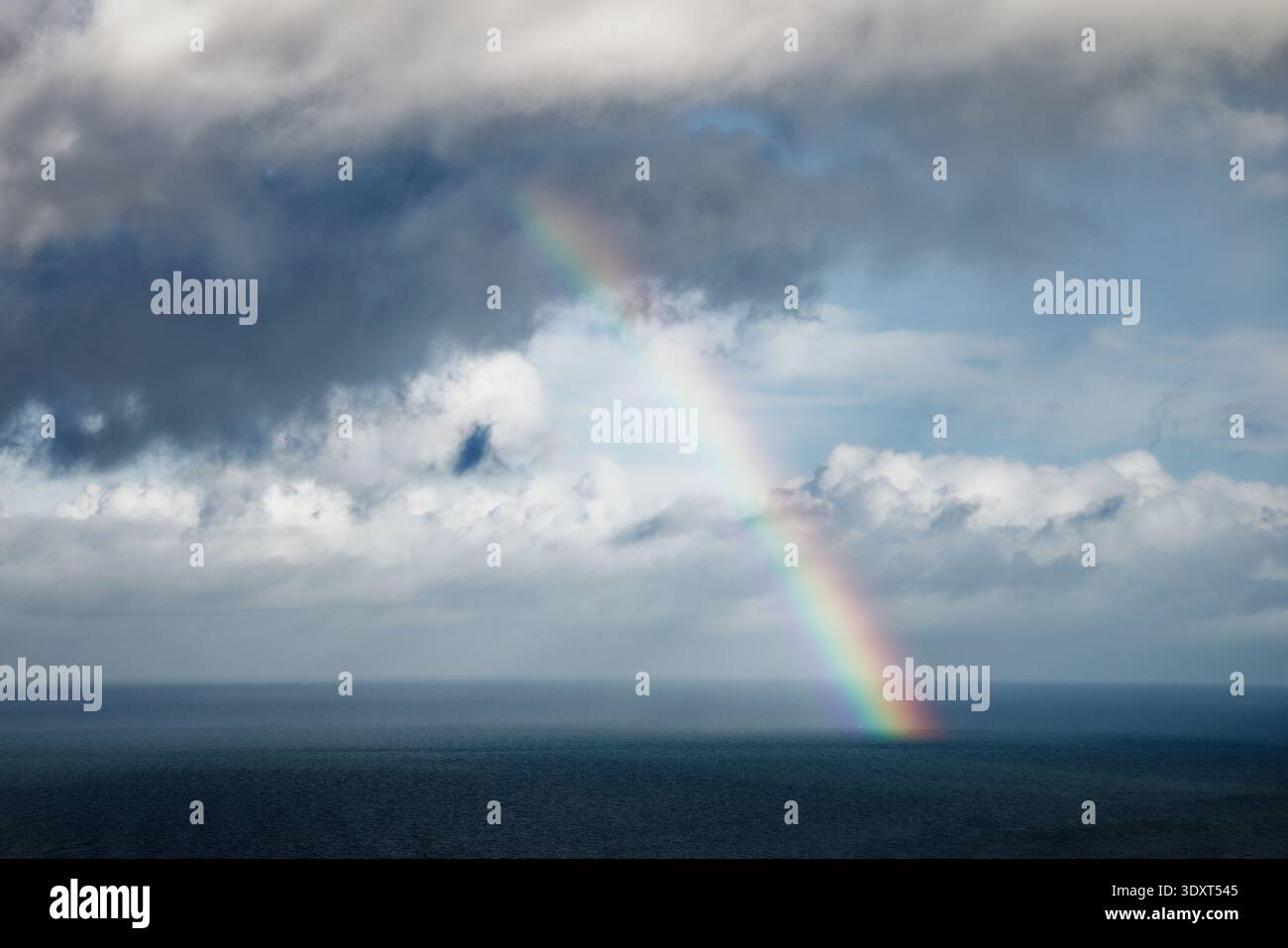 Dunkle Wolken ziehen Regen über ein dunkelgraues Meer, mit einem hellen Regenbogen, der ins Wasser taucht, Great Orme, Llandudno, Nordwales. Stockfoto