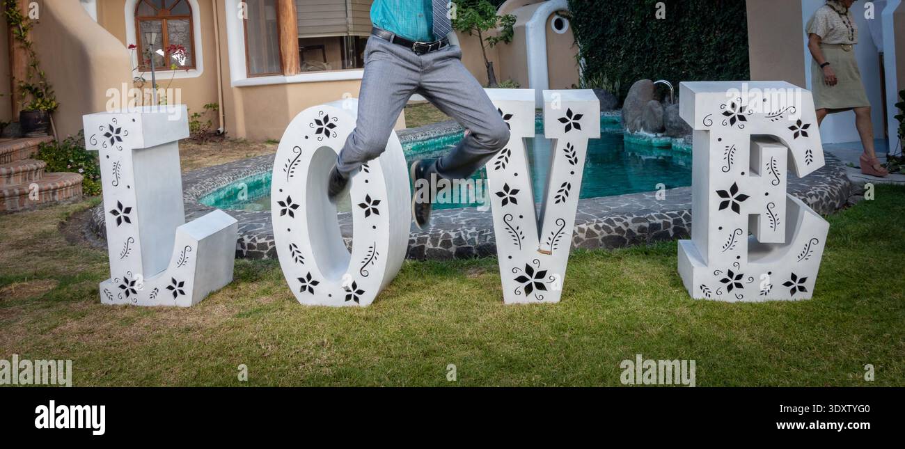 Große dekorative „LOVE“-Buchstaben, die an einem Hochzeitsort im Freien mit Garten und Swimmingpool im Hintergrund ausgestellt werden. Romantische Veranstaltungsdekoration verwendet Stockfoto