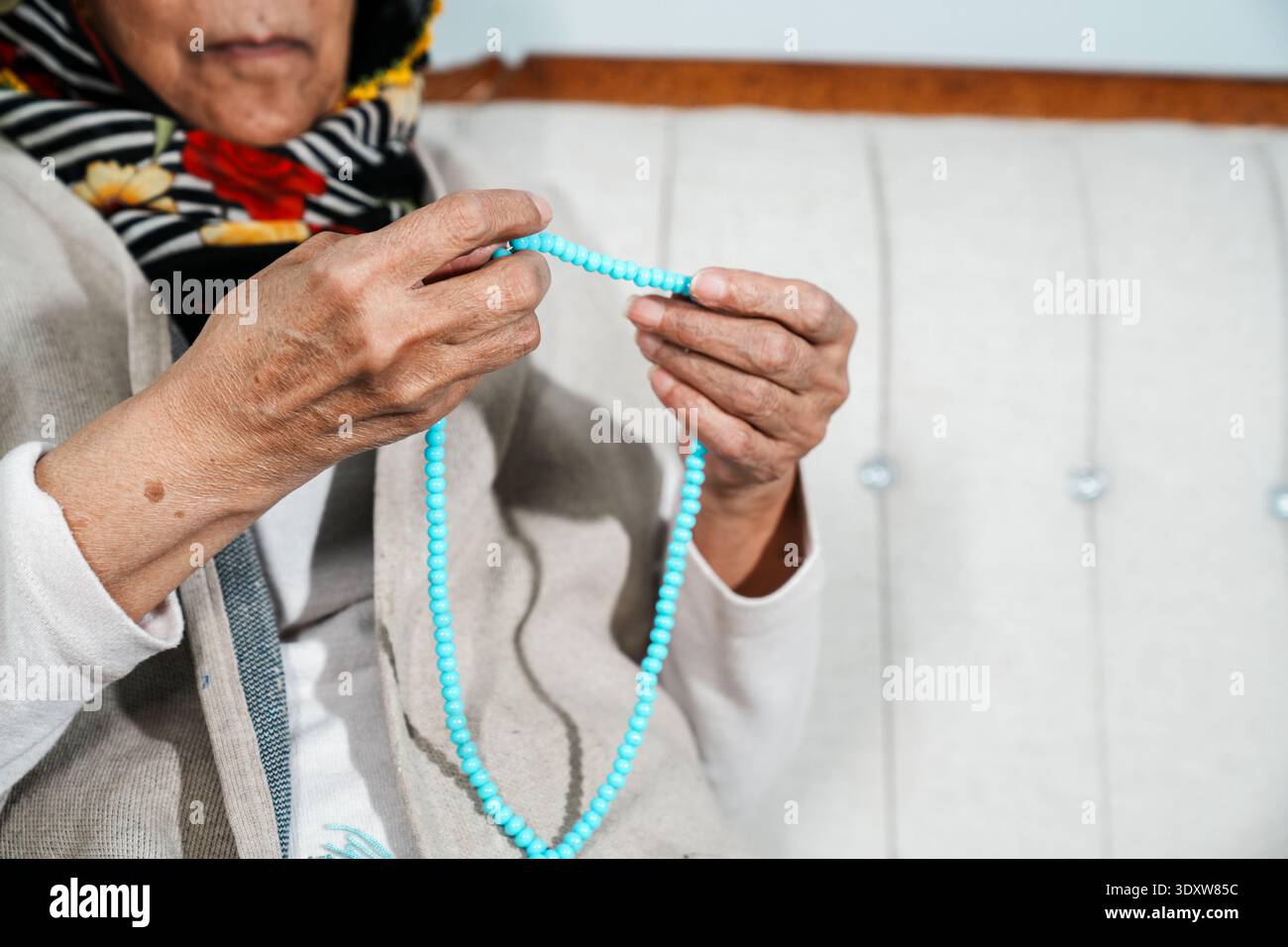 Nahaufnahmen einer älteren muslimischen Frau, die türkisfarbene Gebetsperlen hält und zählt (Tasbih). Vorstellung von Glauben, Hingabe und muslimischem Lebensstil. Stockfoto