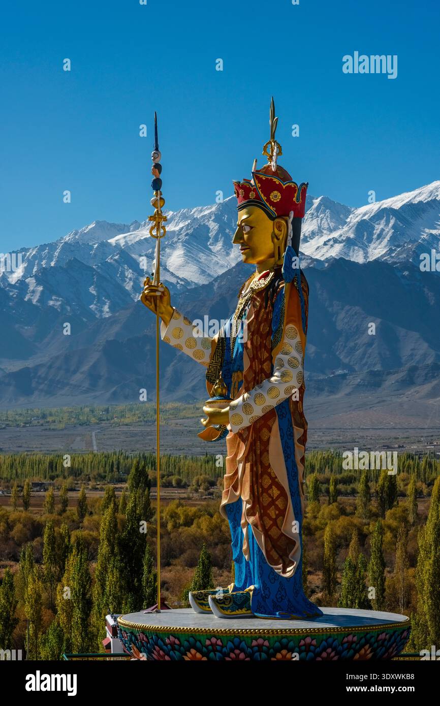 Ein durchgehendes Profil der farbenfrohen Guru Padmasambhava-Statue in Shey überblickt ein Tal aus Herbstbäumen mit hohen Berggipfeln in der Ferne. Stockfoto