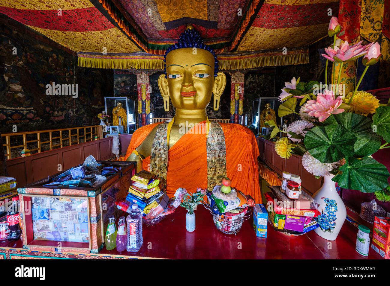 Opfergaben und rituelle Gegenstände werden vor dem monumentalen vergoldeten Shakyamuni Buddha Kopf in der Hauptversammlungshalle in Shey platziert. Stockfoto
