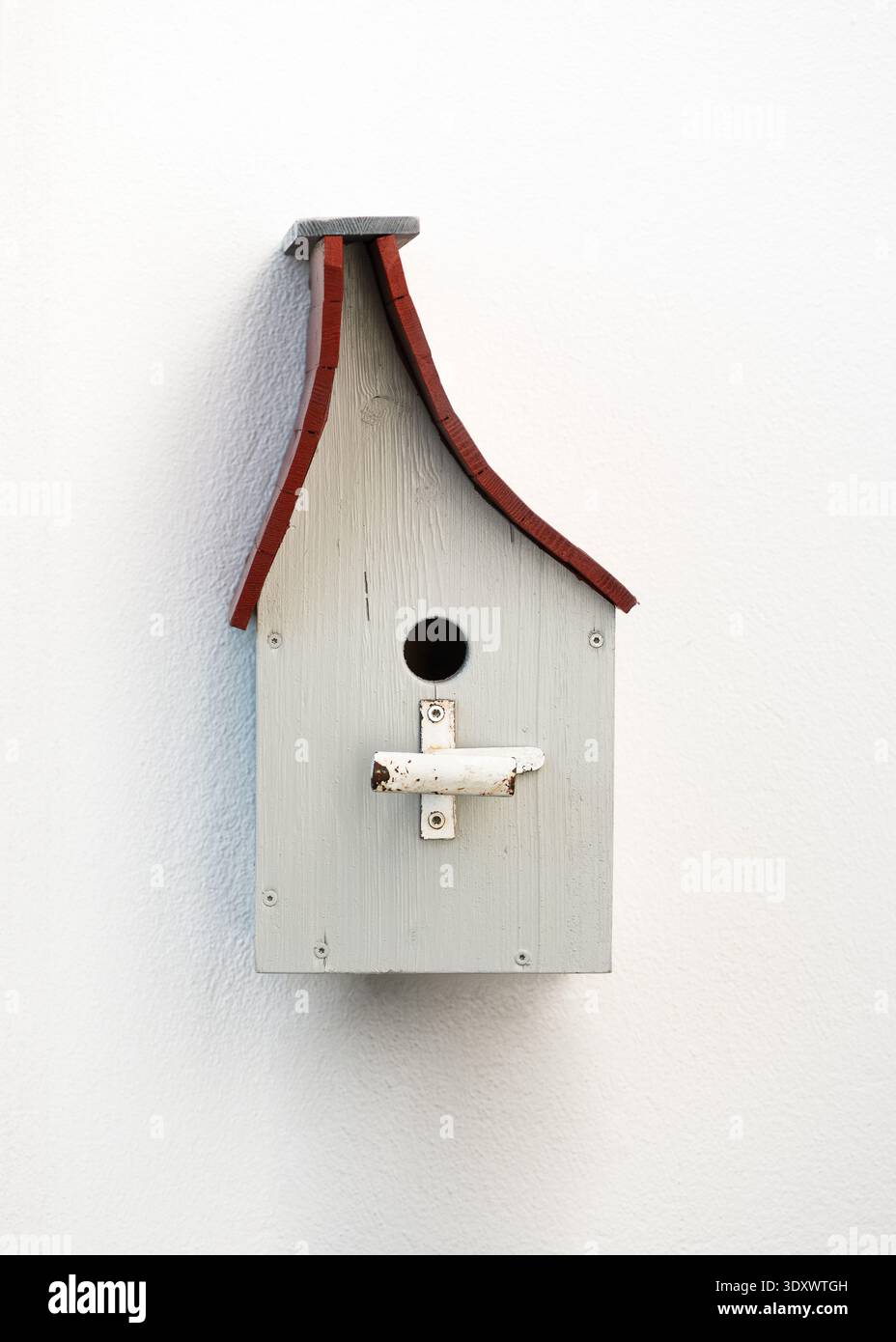 Traditionelles hölzernes Vogelhaus mit rotem Dach an einer weißen Wand. Handgefertigte Nistbox für Gartenvögel, einfaches und rustikales Design. Stockfoto