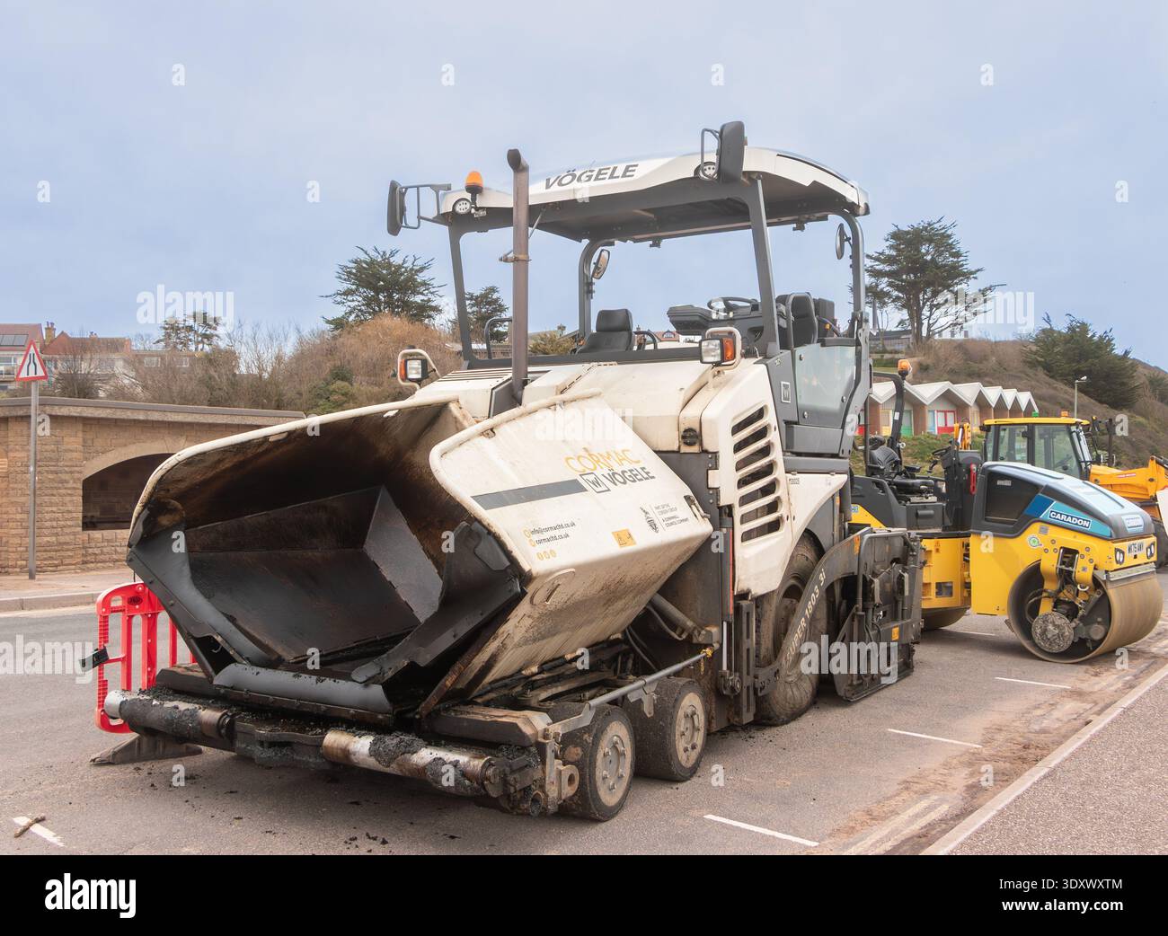 Große Asphaltfertigungsmaschine neben einer gelben Vibrationswalze bei Straßeninstandhaltungsarbeiten in großbritannien, exmouth devon Stockfoto