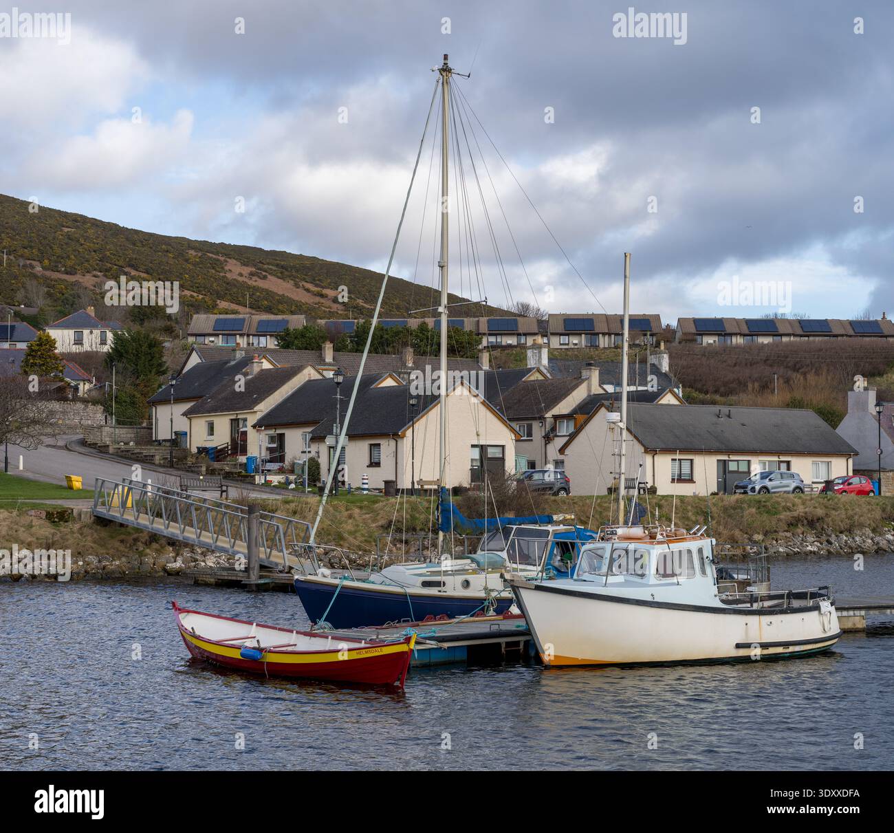 Drei Boote ruhen ruhig im Hafen von Helmsdale. Ein weißes Fischerboot, ein blaues Segelboot und ein kleines rotes Ruderboot sind am Dock gebunden. Stockfoto